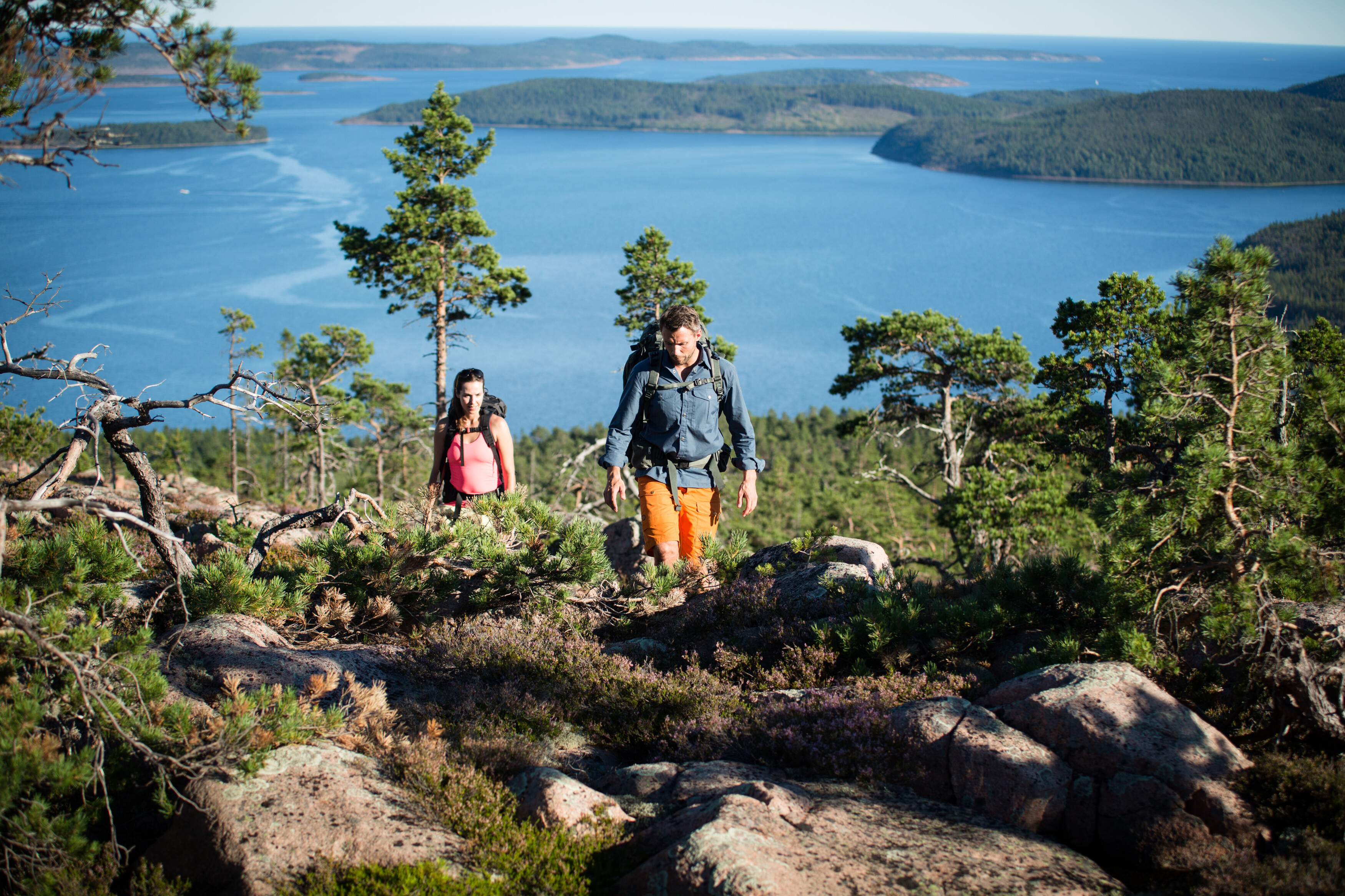Två personer vandrar uppåt med en sjö i bakgrunden